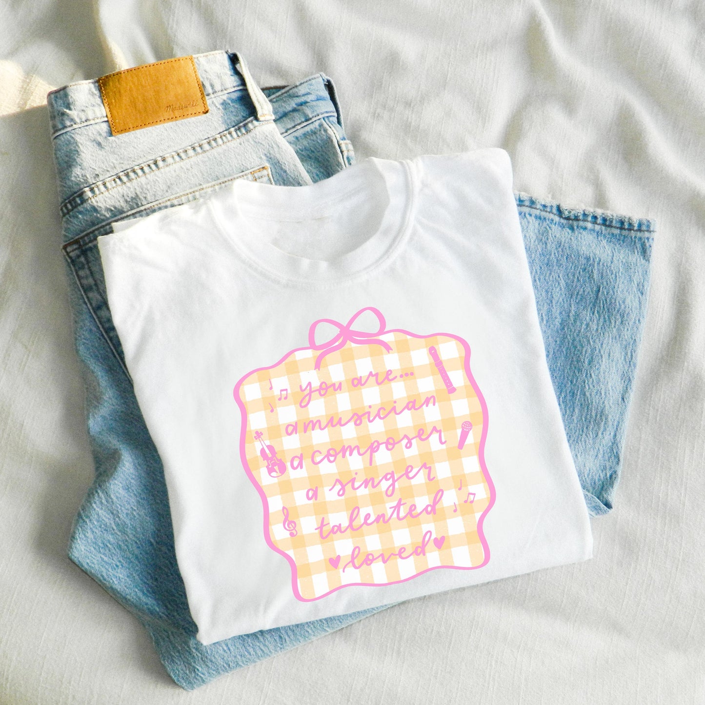 White elementary music teacher t-shirt with colorful graphic design and blue jeans on a light background
