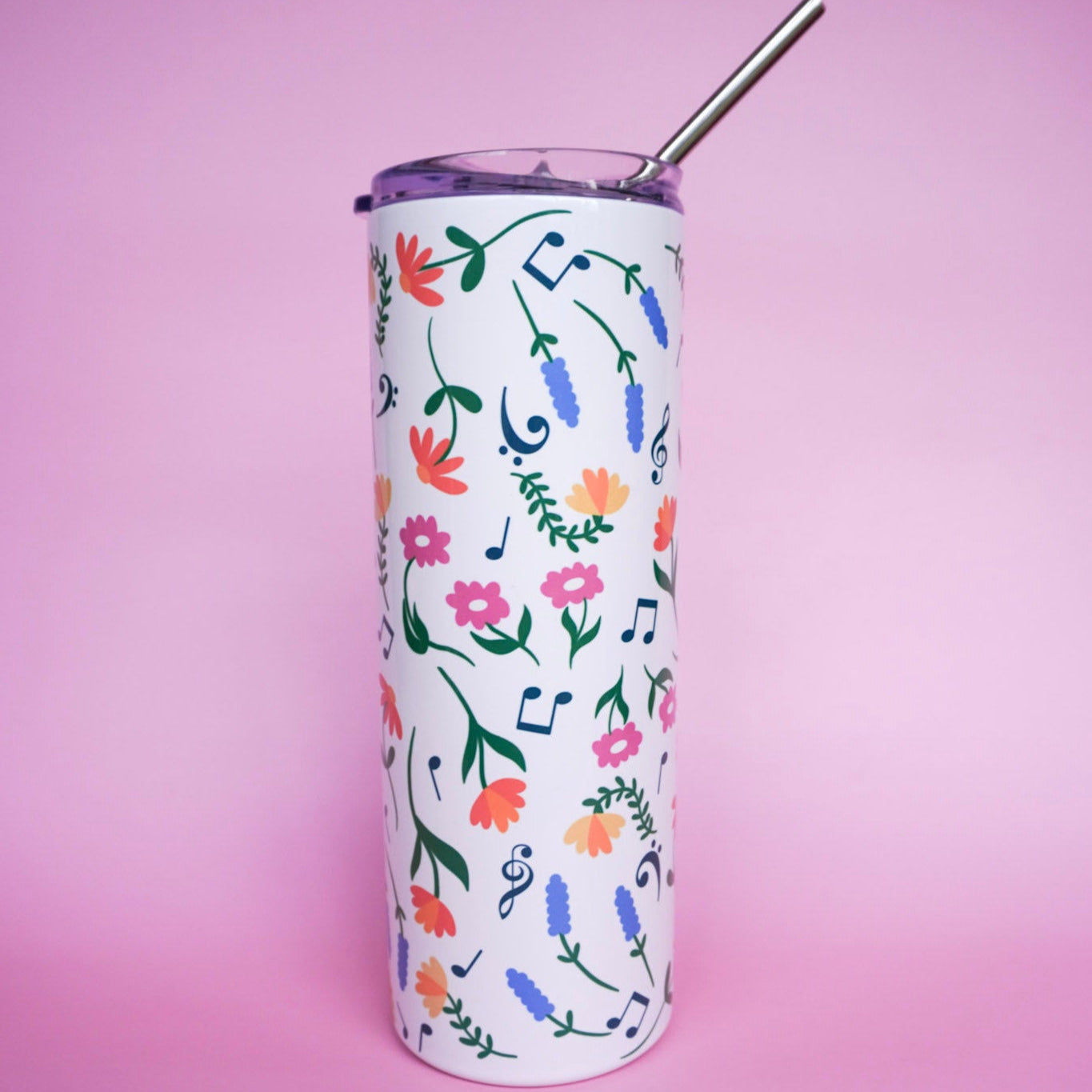 Tumbler with floral design with music notes and metal straw on a pink background.