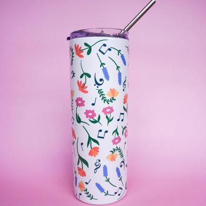 Tumbler with floral design with music notes and metal straw on a pink background.
