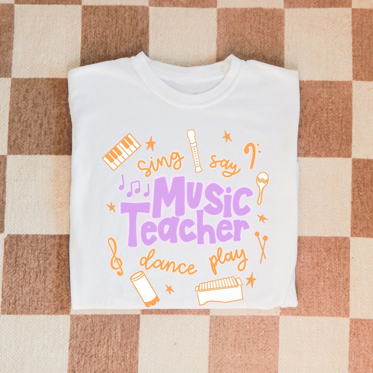 Music Teacher Shirt. A white shirt with the words Music Teacher, Sing, Say, Dance, Play, and drawings of musical instruments.