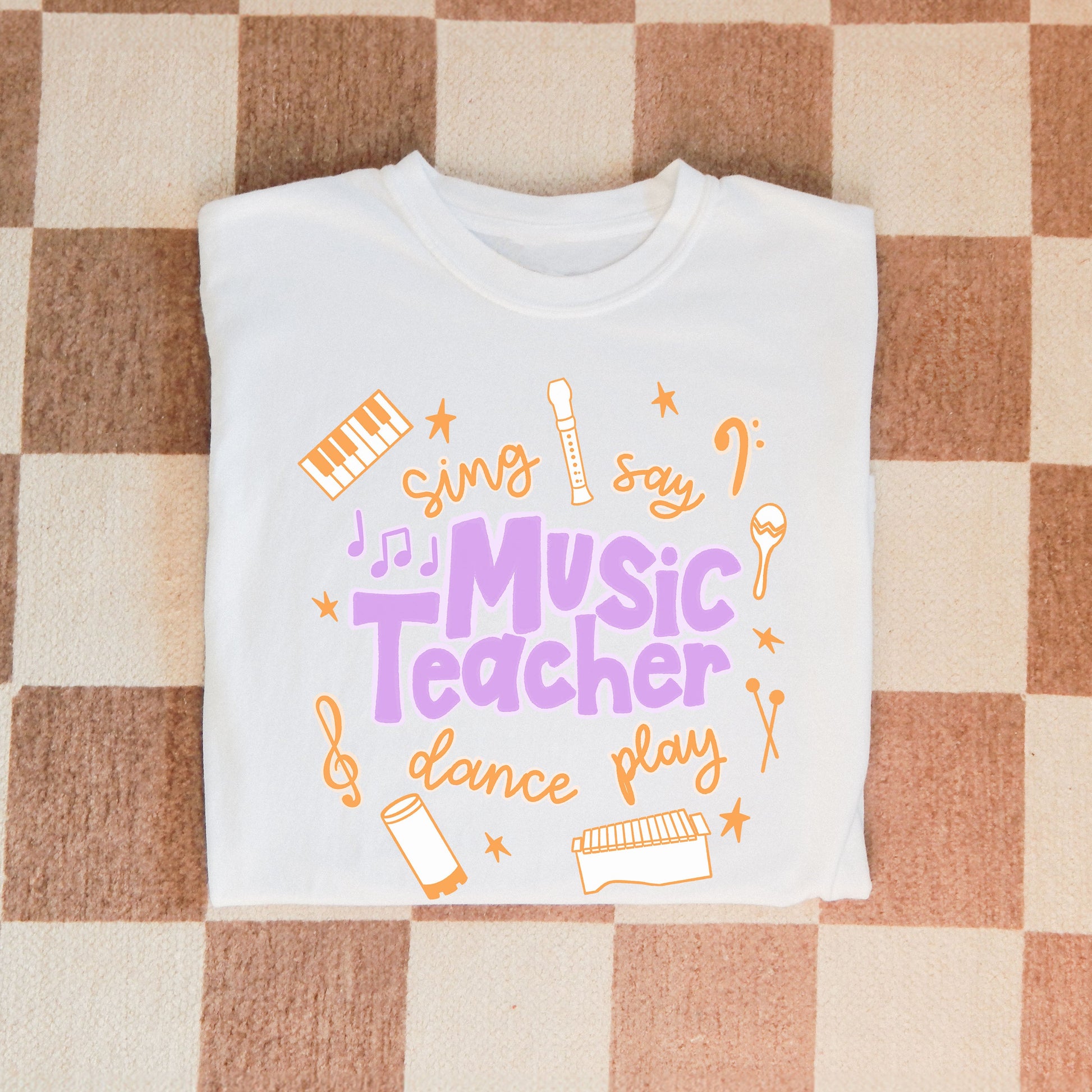 Music Teacher Shirt. A white shirt with the words Music Teacher, Sing, Say, Dance, Play, and drawings of musical instruments.